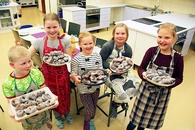 Viisi lasta pitelee tarjottimia, joilla on sokerimunkkeja.